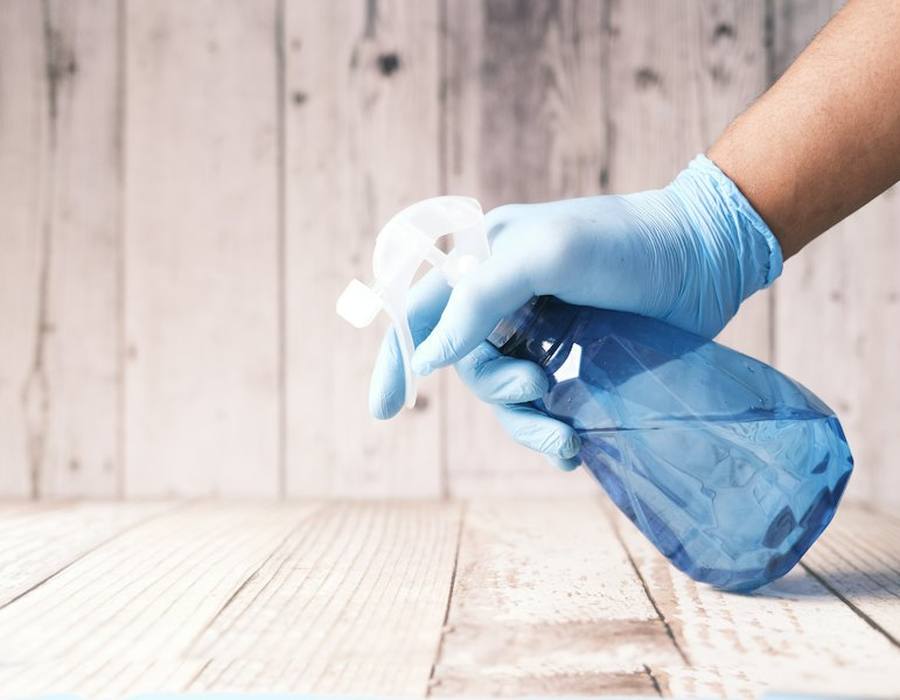 Gloved hand holding a spray bottle of cleaner